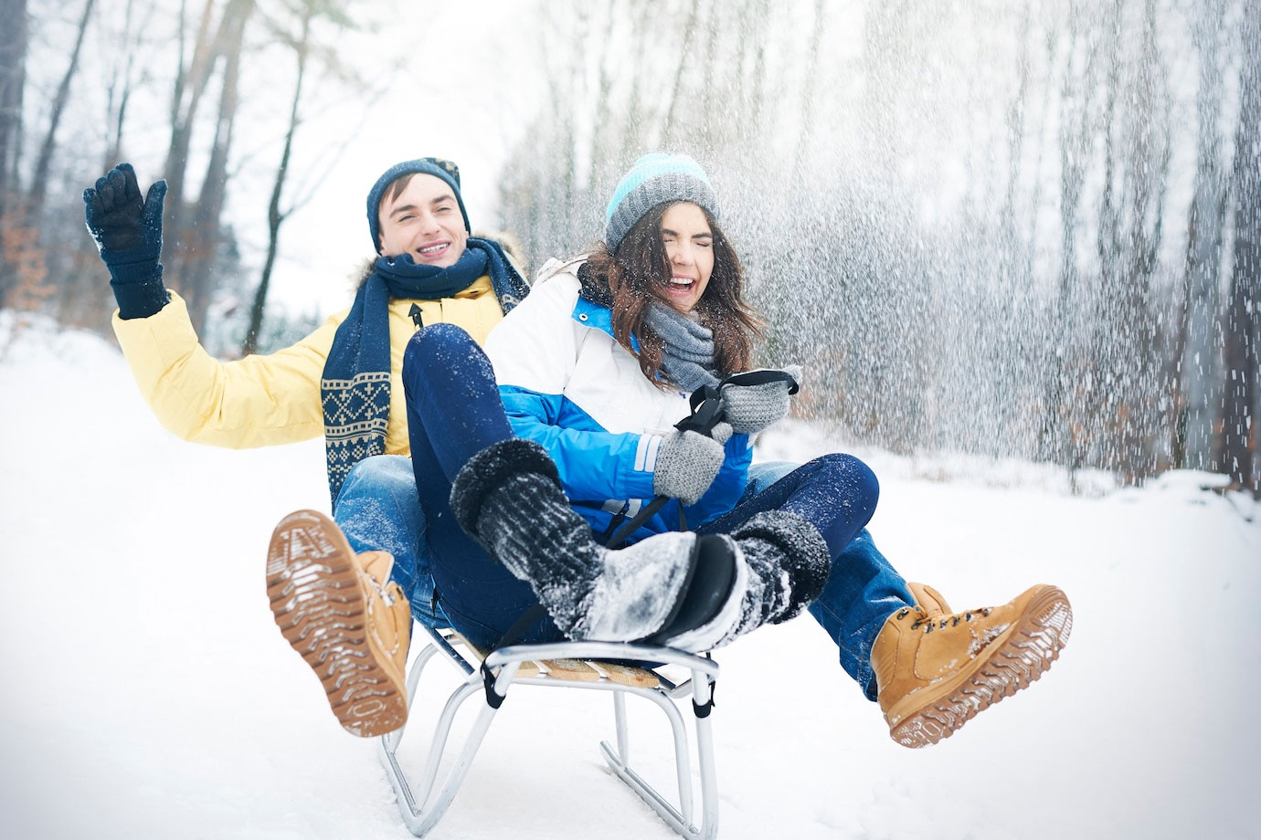 Image shows a young man and woman sledding in the snow. 